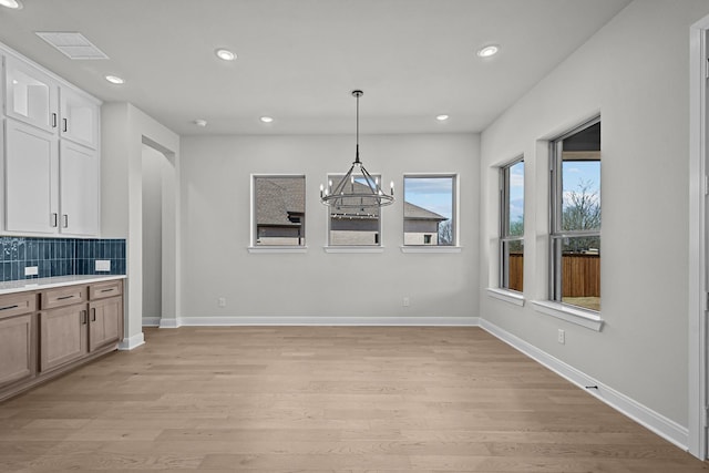 unfurnished dining area featuring visible vents, baseboards, light wood finished floors, recessed lighting, and a notable chandelier