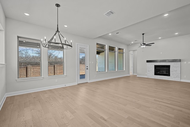 unfurnished living room with light wood-type flooring, ceiling fan with notable chandelier, recessed lighting, a fireplace, and baseboards