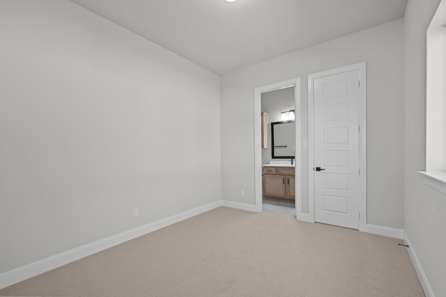 unfurnished bedroom featuring baseboards, light carpet, and ensuite bathroom