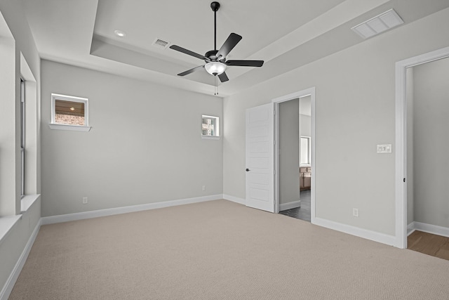 unfurnished bedroom featuring a tray ceiling, baseboards, visible vents, and ensuite bathroom