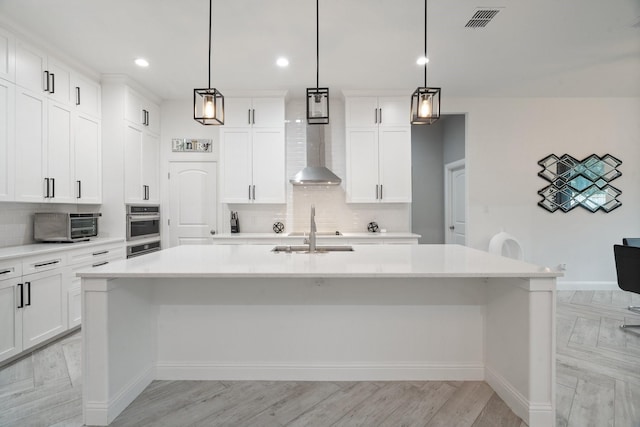 kitchen featuring hanging light fixtures, light wood-type flooring, decorative backsplash, and a kitchen island with sink