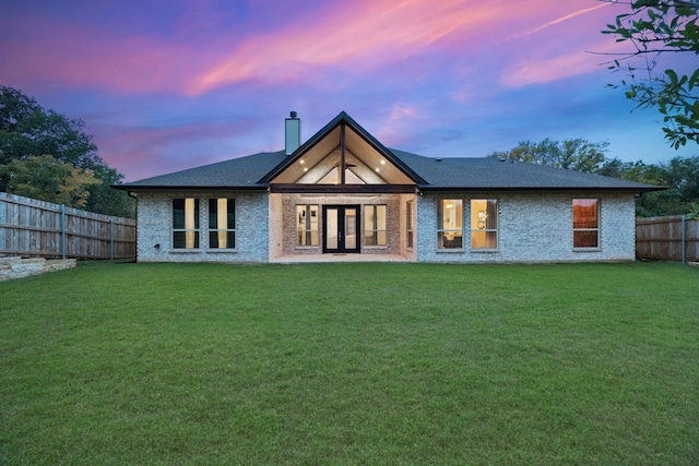 back house at dusk featuring french doors and a lawn