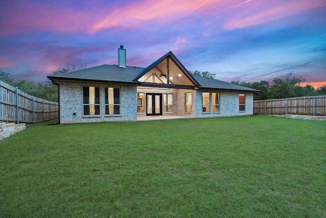 back house at dusk featuring a lawn