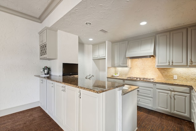 kitchen featuring custom exhaust hood, kitchen peninsula, stainless steel gas cooktop, dark hardwood / wood-style floors, and dark stone countertops