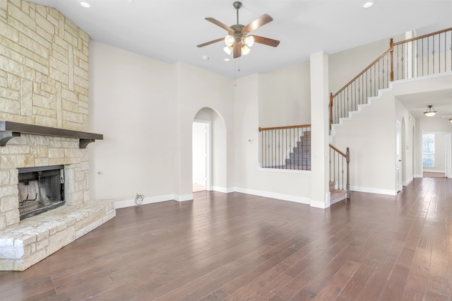 unfurnished living room with ceiling fan, a fireplace, dark hardwood / wood-style floors, and a high ceiling