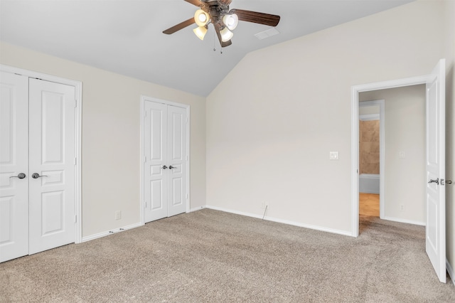 unfurnished bedroom with ceiling fan, vaulted ceiling, light carpet, and two closets