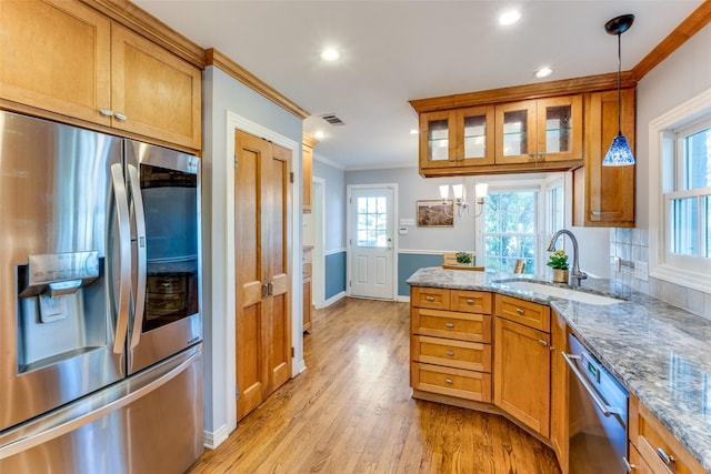 kitchen with light stone counters, stainless steel appliances, sink, decorative light fixtures, and light hardwood / wood-style flooring