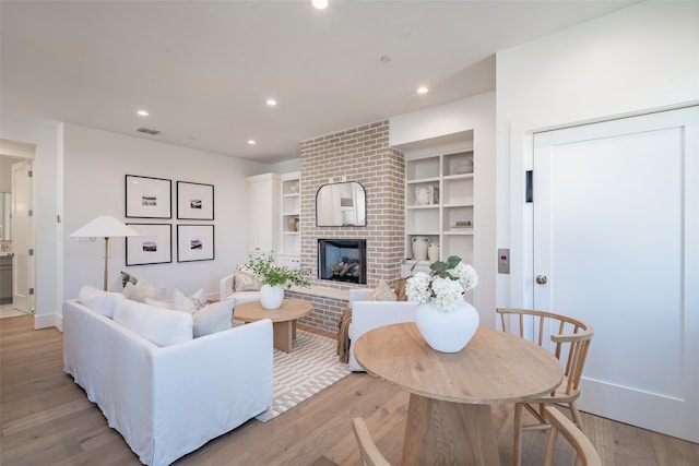 living room with a fireplace, built in shelves, and light hardwood / wood-style flooring