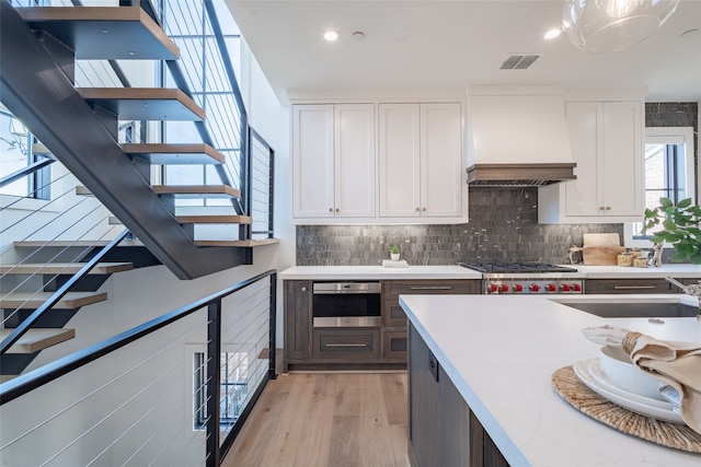 kitchen featuring light hardwood / wood-style floors, premium range hood, stainless steel appliances, and white cabinets