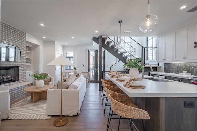 living room featuring built in shelves, light hardwood / wood-style flooring, a brick fireplace, and sink