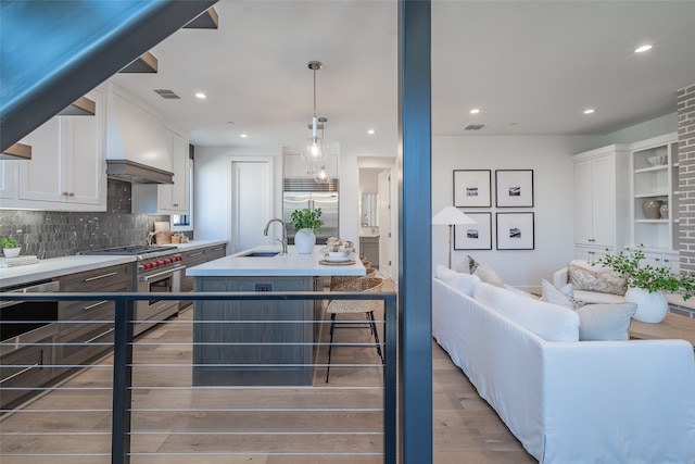 kitchen featuring an island with sink, hardwood / wood-style floors, white cabinets, high end appliances, and sink