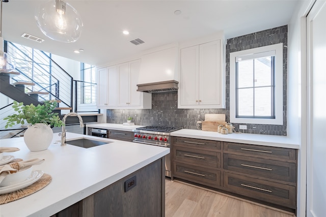 kitchen featuring custom exhaust hood, high end stainless steel range, sink, and white cabinets