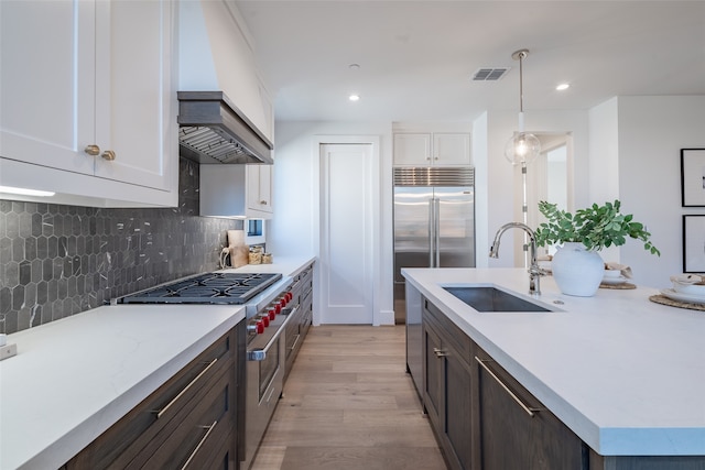 kitchen featuring light wood-type flooring, high end stainless steel range oven, sink, premium range hood, and white cabinetry