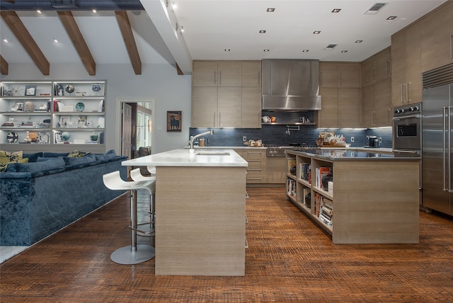 kitchen featuring a center island with sink, wall chimney range hood, a kitchen breakfast bar, stainless steel appliances, and decorative backsplash