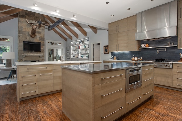 kitchen featuring wall chimney exhaust hood, decorative backsplash, appliances with stainless steel finishes, vaulted ceiling with beams, and a center island