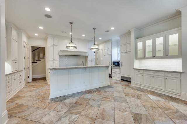 kitchen with white cabinets, a kitchen island with sink, hanging light fixtures, and tasteful backsplash