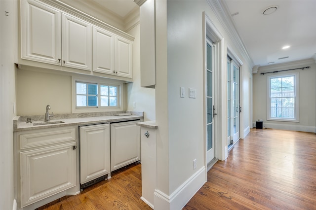 kitchen with light stone countertops, sink, white cabinetry, light hardwood / wood-style flooring, and ornamental molding