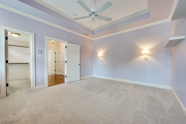 unfurnished bedroom featuring a walk in closet, ceiling fan, crown molding, light carpet, and a raised ceiling