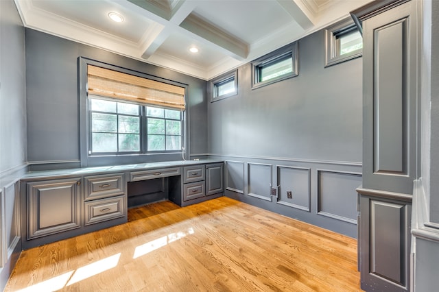 unfurnished office with beamed ceiling, built in desk, light hardwood / wood-style floors, crown molding, and coffered ceiling