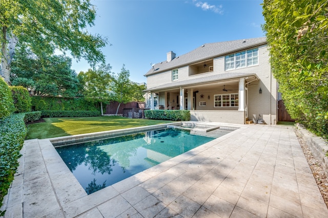 rear view of property featuring ceiling fan, a pool with hot tub, a patio, and a lawn