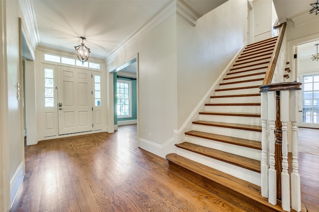 foyer entrance with a healthy amount of sunlight, crown molding, hardwood / wood-style floors, and an inviting chandelier