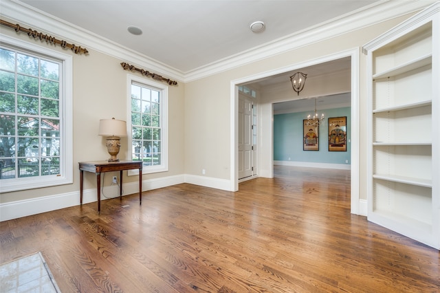 unfurnished room featuring built in features, crown molding, hardwood / wood-style floors, and a notable chandelier