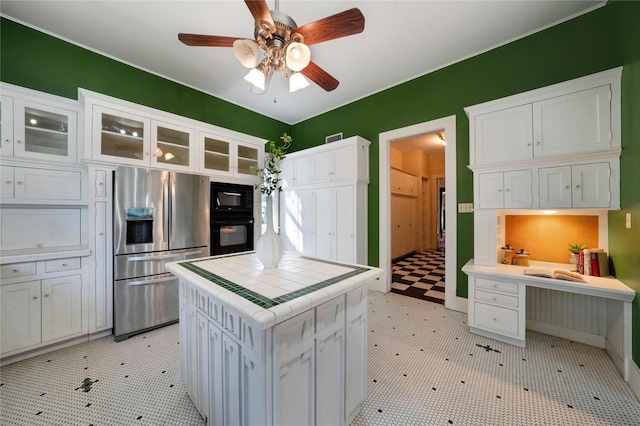 kitchen featuring tile countertops, light floors, glass insert cabinets, white cabinetry, and black appliances