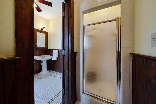 bathroom featuring a stall shower, wooden walls, a ceiling fan, and a wainscoted wall