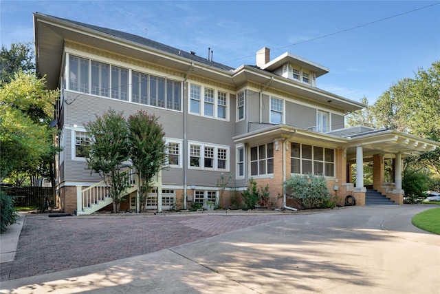 exterior space featuring decorative driveway, brick siding, a chimney, stairway, and a sunroom