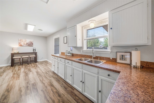 kitchen with white cabinetry, sink, and wood-type flooring