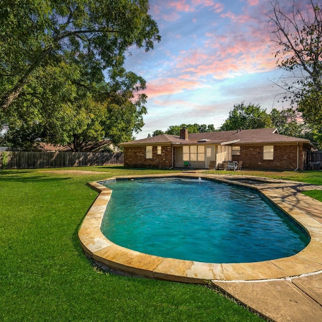 pool at dusk with a patio area and a lawn