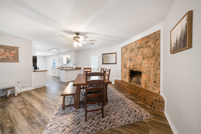 dining area featuring ceiling fan, dark hardwood / wood-style flooring, and a stone fireplace