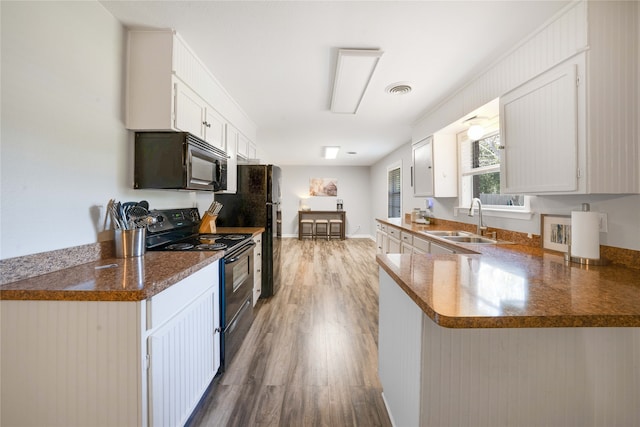 kitchen featuring sink, kitchen peninsula, white cabinetry, black appliances, and hardwood / wood-style flooring