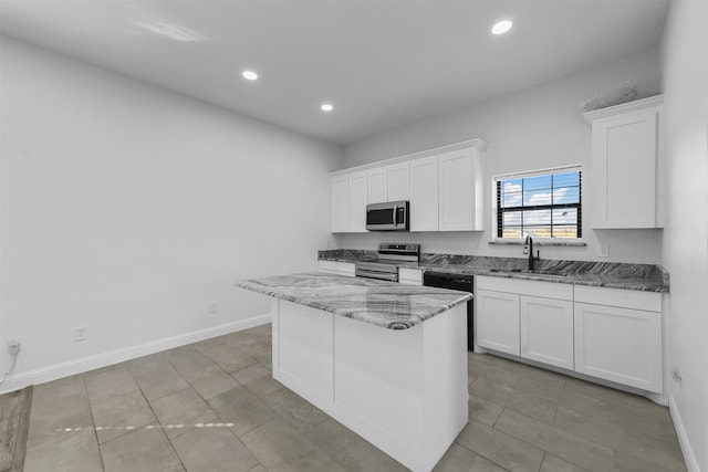 kitchen with white cabinets, light stone countertops, stainless steel appliances, and a kitchen island