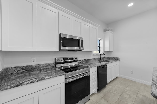 kitchen with stainless steel appliances, dark stone counters, sink, light tile patterned flooring, and white cabinets