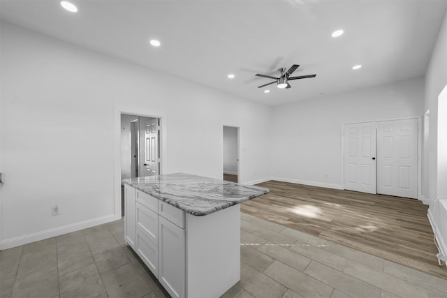 kitchen featuring light wood-type flooring, a center island, white cabinetry, ceiling fan, and light stone counters