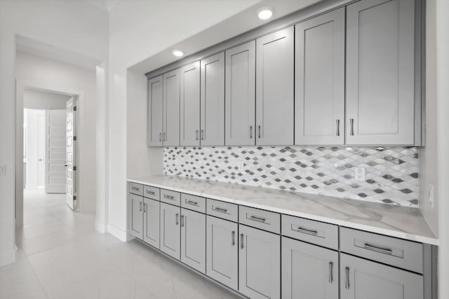 kitchen featuring tasteful backsplash, light stone countertops, and gray cabinets