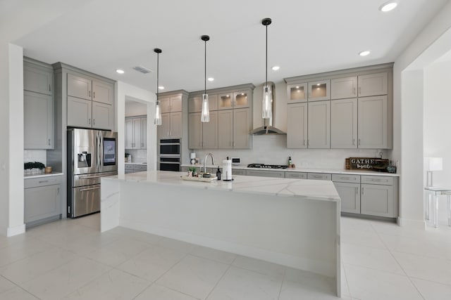 kitchen featuring stainless steel fridge, multiple ovens, gray cabinets, gas cooktop, and wall chimney range hood