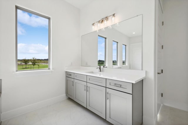 bathroom with baseboards, a healthy amount of sunlight, marble finish floor, and vanity