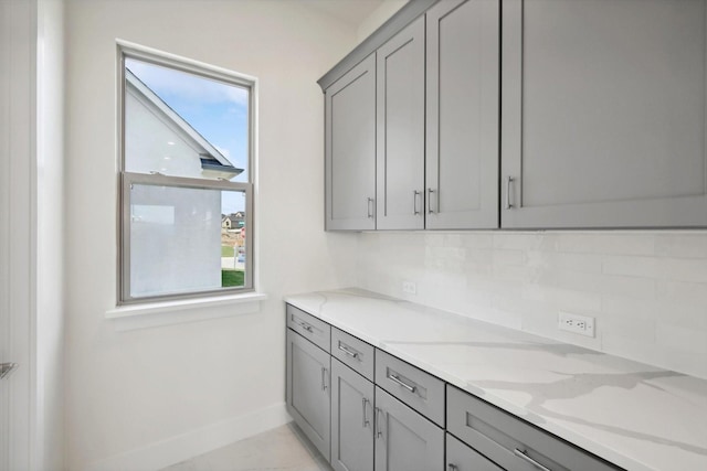 kitchen featuring gray cabinetry, baseboards, light stone countertops, and tasteful backsplash
