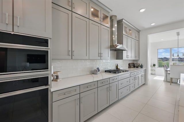 kitchen with gray cabinetry, wall chimney range hood, oven, and decorative backsplash
