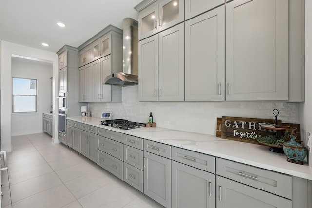 kitchen featuring gray cabinetry, stainless steel gas cooktop, backsplash, and wall chimney range hood