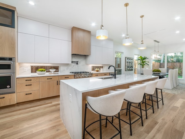 kitchen featuring a center island with sink, decorative light fixtures, white cabinetry, and light hardwood / wood-style flooring