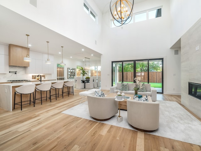 living room featuring sink, a towering ceiling, a fireplace, light hardwood / wood-style floors, and a chandelier