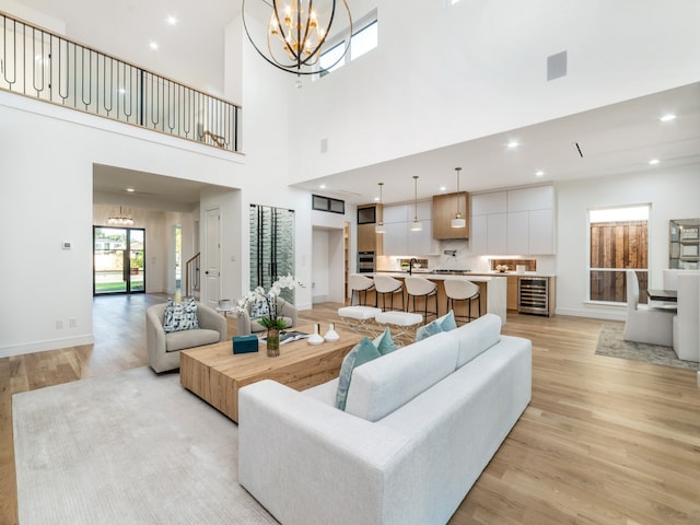 living room featuring light hardwood / wood-style floors, a towering ceiling, wine cooler, and an inviting chandelier