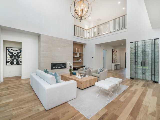 living room with a fireplace, an inviting chandelier, a high ceiling, and light wood-type flooring