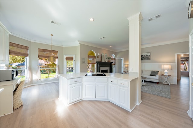 kitchen featuring hanging light fixtures, kitchen peninsula, decorative columns, and white cabinetry