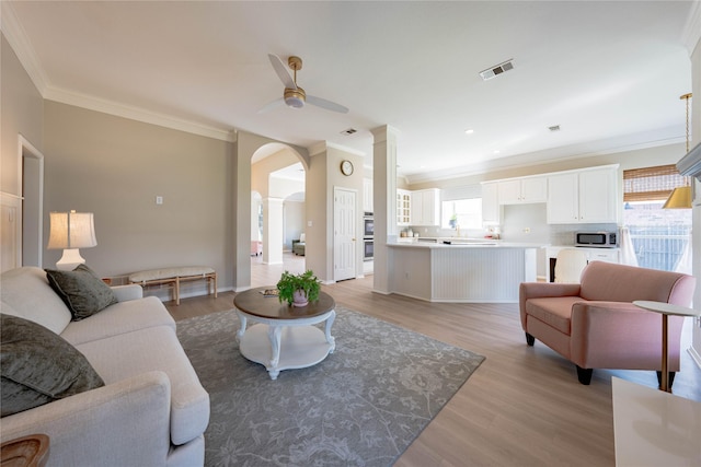 living room featuring a wealth of natural light, ceiling fan, crown molding, and arched walkways