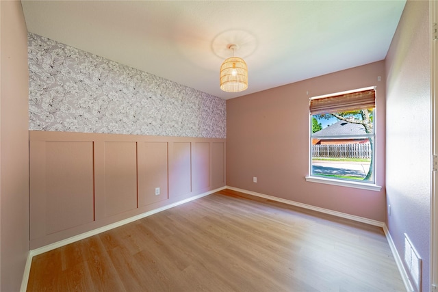 unfurnished room with visible vents, wainscoting, light wood-style floors, and wallpapered walls