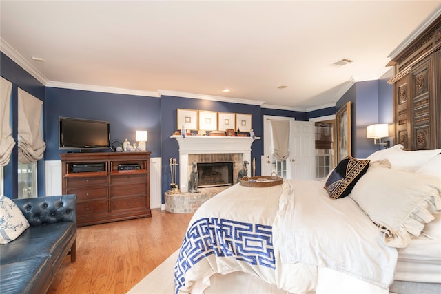 bedroom featuring light wood-type flooring, crown molding, and a fireplace